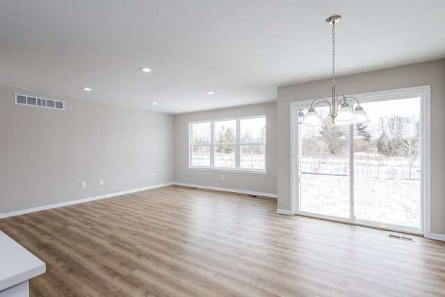 unfurnished dining area with visible vents, a notable chandelier, baseboards, and wood finished floors