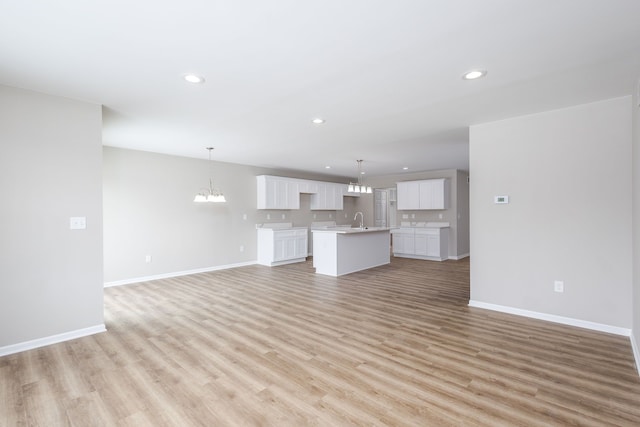 unfurnished living room featuring baseboards, a sink, light wood-style flooring, and an inviting chandelier