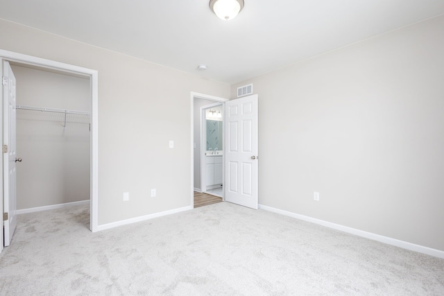 unfurnished bedroom with a walk in closet, carpet flooring, visible vents, and baseboards