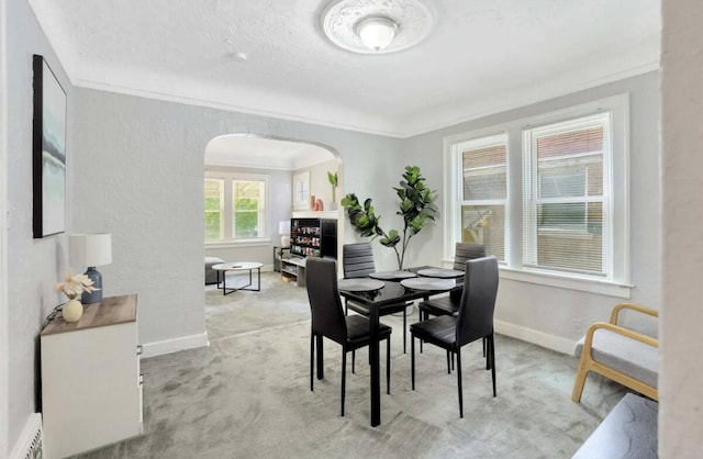 dining room with carpet, crown molding, arched walkways, and baseboards