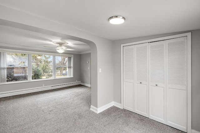 unfurnished bedroom featuring arched walkways, light carpet, baseboards, baseboard heating, and a closet