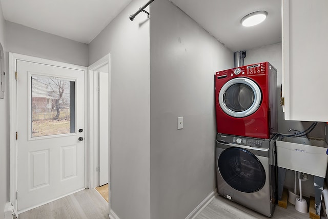 washroom with laundry area, baseboards, stacked washer / drying machine, wood finished floors, and a sink