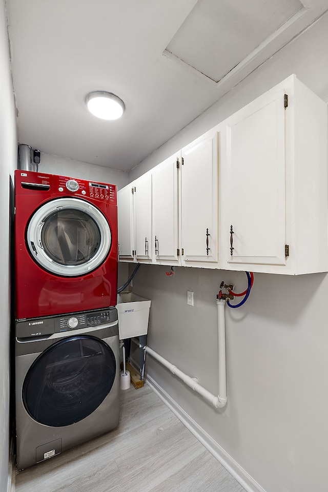 laundry room with cabinet space, baseboards, stacked washer and clothes dryer, wood finished floors, and a sink