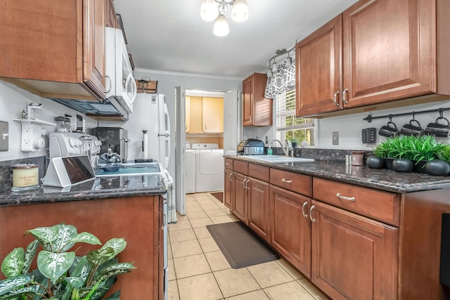 kitchen with light tile patterned flooring, a sink, independent washer and dryer, dark stone counters, and brown cabinetry