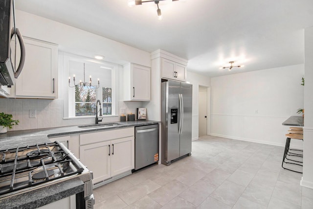 kitchen with dark countertops, backsplash, appliances with stainless steel finishes, white cabinetry, and a sink