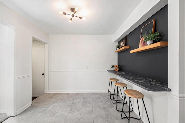 kitchen with dark stone countertops, wainscoting, a kitchen bar, and open shelves