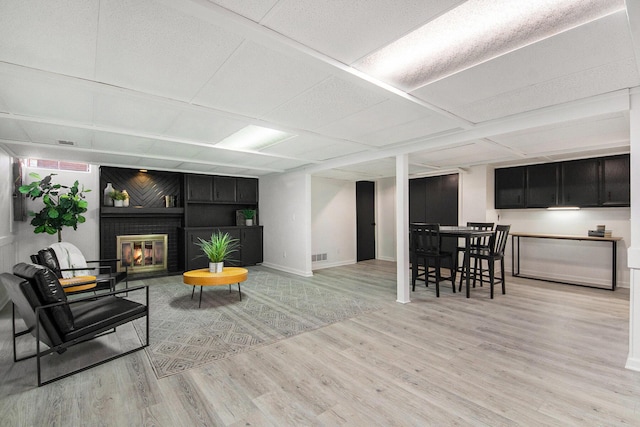 living room with light wood finished floors, a brick fireplace, a paneled ceiling, and baseboards