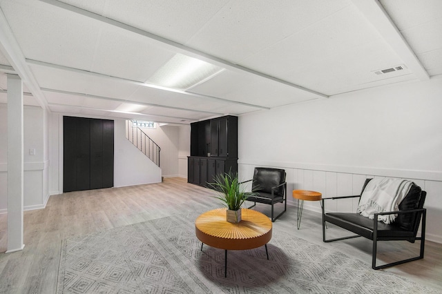 living area featuring light wood-style floors, stairway, visible vents, and a wainscoted wall