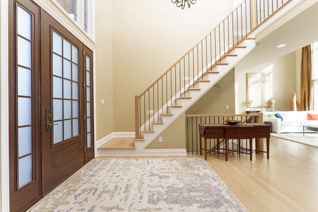 foyer entrance featuring stairway, baseboards, a towering ceiling, and wood finished floors