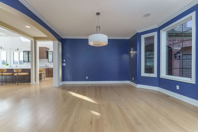 interior space featuring baseboards, arched walkways, light wood-type flooring, and ornamental molding