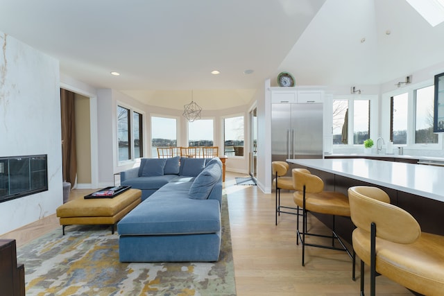 living area featuring recessed lighting, light wood-style floors, an inviting chandelier, a skylight, and baseboards