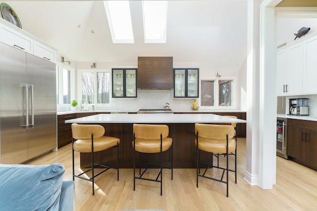 kitchen featuring light countertops, custom range hood, backsplash, and built in refrigerator