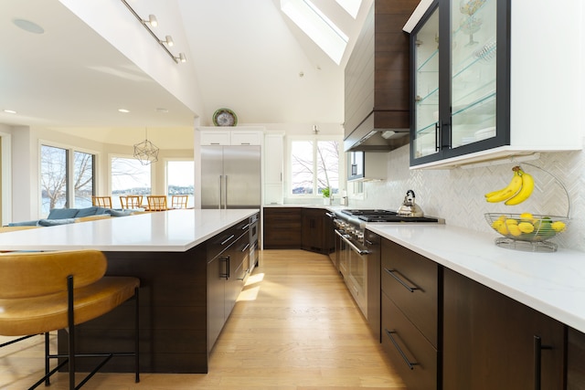 kitchen featuring glass insert cabinets, dark brown cabinetry, a breakfast bar, premium appliances, and decorative backsplash