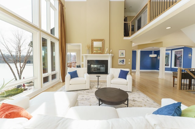 living area with baseboards, a high ceiling, wood finished floors, a glass covered fireplace, and ornate columns