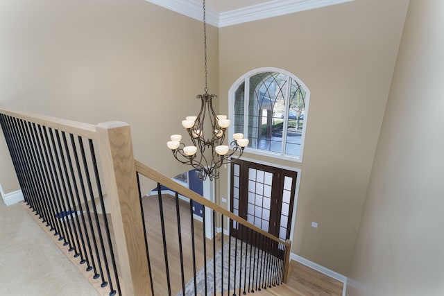 stairs featuring wood finished floors, baseboards, ornamental molding, a towering ceiling, and a chandelier