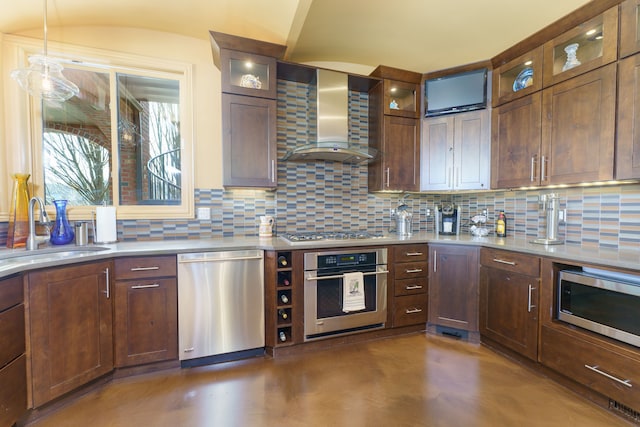 kitchen featuring concrete flooring, decorative backsplash, stainless steel appliances, wall chimney exhaust hood, and a sink