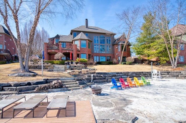 back of house featuring a balcony, a patio area, a chimney, and an outdoor fire pit