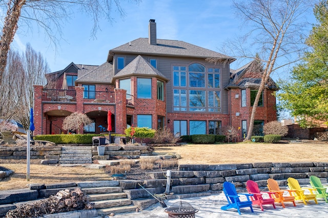 back of property with a patio, a fire pit, brick siding, and a chimney