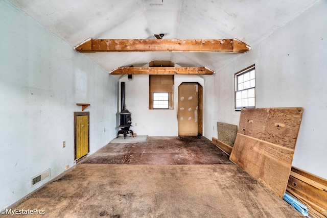 unfurnished room with vaulted ceiling, a wealth of natural light, visible vents, and a wood stove