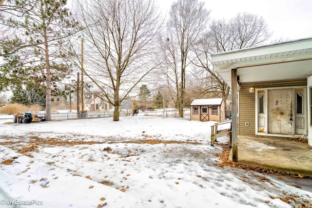 yard layered in snow featuring a storage unit, fence, and an outdoor structure