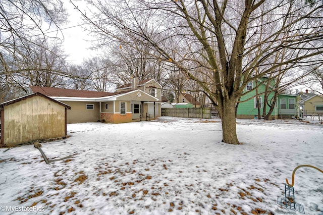 snow covered rear of property featuring a chimney, fence, and an outbuilding