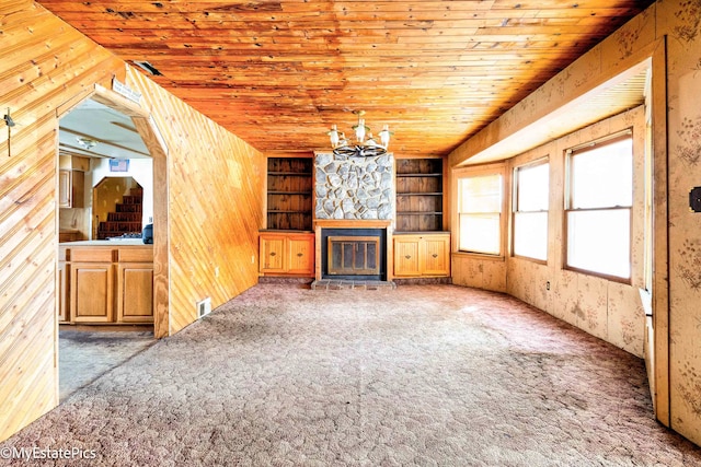 unfurnished living room with wood ceiling, carpet, a stone fireplace, wood walls, and a notable chandelier