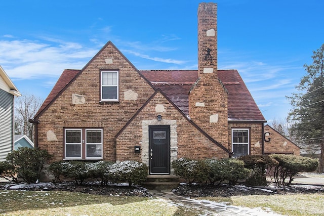 tudor-style house featuring a shingled roof and brick siding