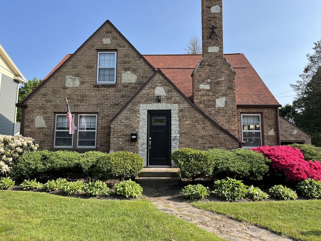 tudor-style house featuring a chimney and brick siding