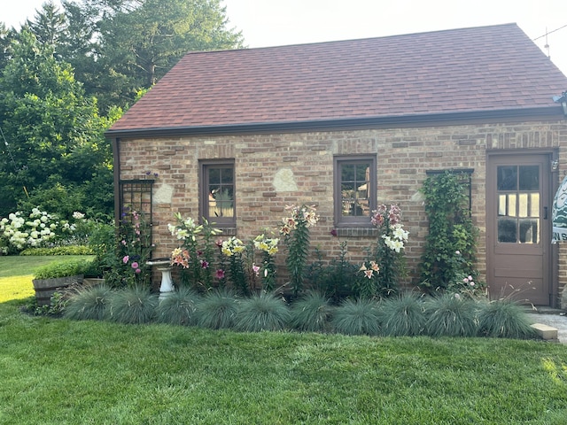 view of property exterior with a shingled roof, a lawn, and brick siding