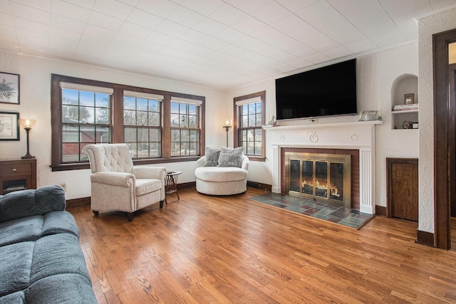 living room featuring baseboards, a glass covered fireplace, wood finished floors, and crown molding