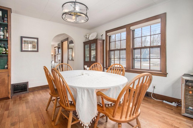 dining room featuring arched walkways, light wood finished floors, visible vents, ornamental molding, and a chandelier