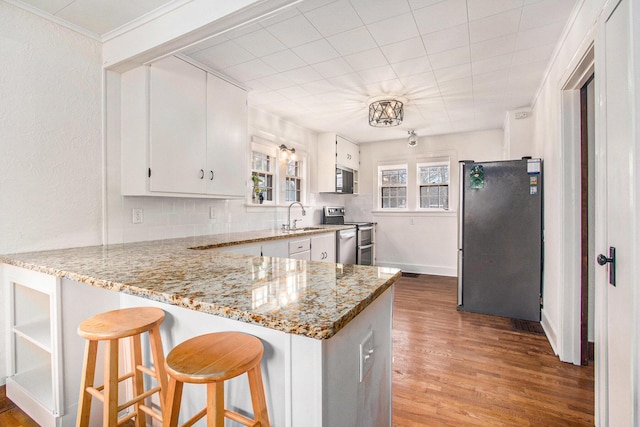 kitchen featuring stainless steel appliances, a peninsula, wood finished floors, white cabinetry, and backsplash