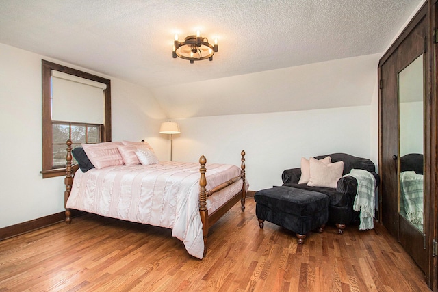 bedroom with light wood-type flooring, vaulted ceiling, a textured ceiling, and baseboards