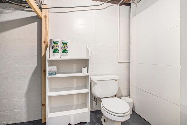 bathroom featuring concrete flooring, concrete block wall, and toilet