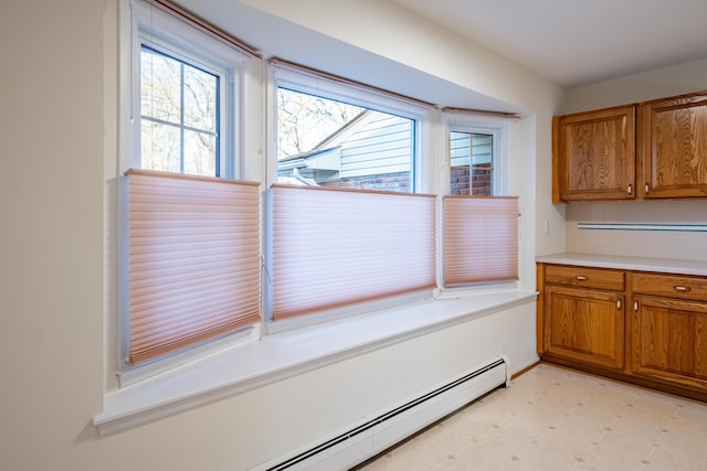 interior space with light floors, brown cabinets, a baseboard radiator, light countertops, and tasteful backsplash