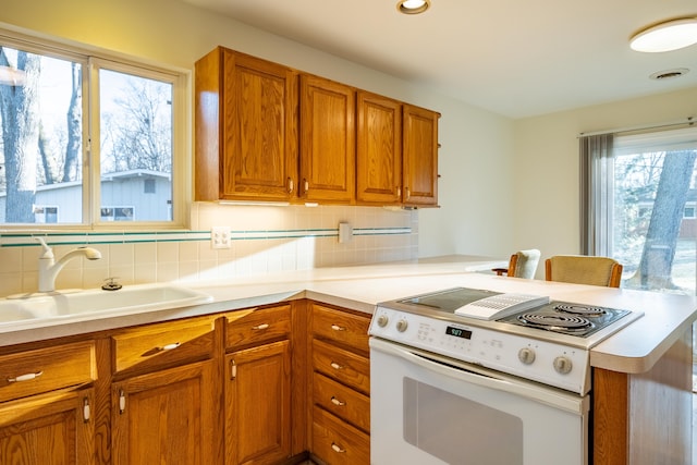 kitchen featuring white electric stove, a peninsula, a sink, decorative backsplash, and brown cabinets