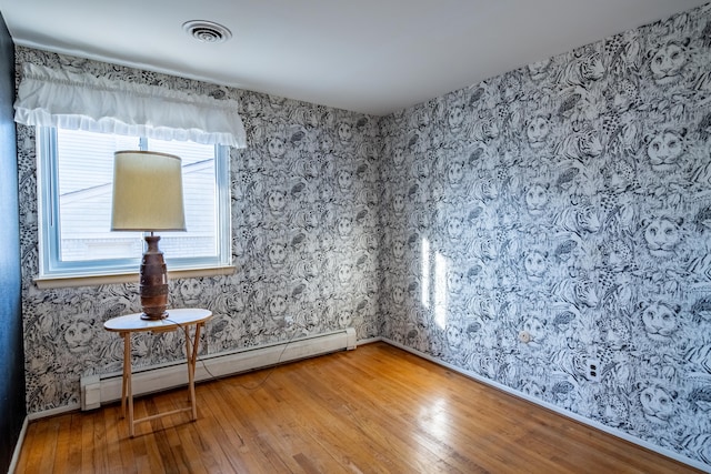 empty room featuring a baseboard heating unit, visible vents, light wood-style flooring, and wallpapered walls