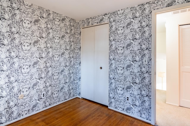 unfurnished bedroom featuring a closet, visible vents, wood finished floors, and wallpapered walls