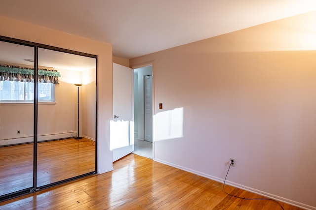 unfurnished bedroom featuring light wood finished floors, baseboards, a closet, and a baseboard radiator