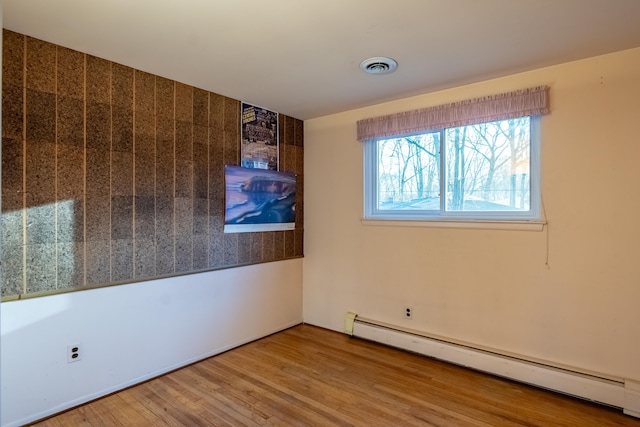 spare room with a baseboard radiator, visible vents, and wood finished floors