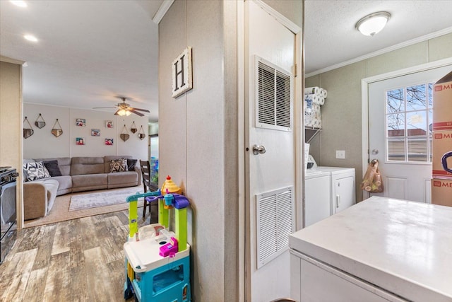 interior space featuring washing machine and dryer, laundry area, wood finished floors, a ceiling fan, and crown molding