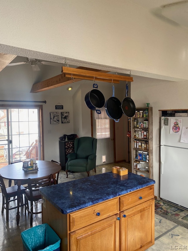 kitchen with dark countertops, a center island, freestanding refrigerator, and a ceiling fan