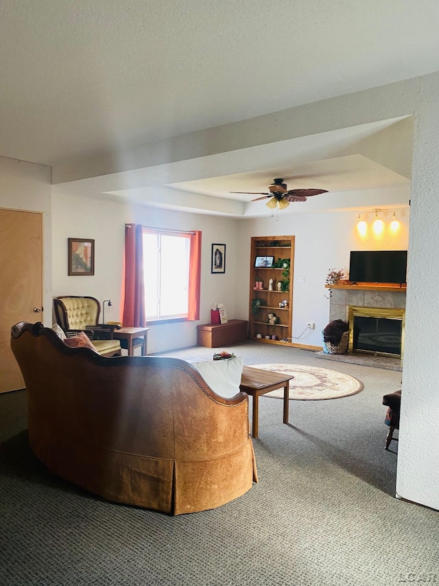 carpeted living room with a ceiling fan, a tray ceiling, and a tiled fireplace