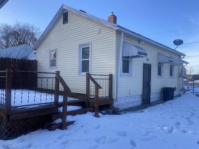 snow covered rear of property featuring a chimney and fence