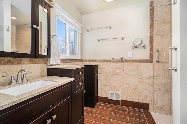 full bathroom featuring visible vents, tile walls, vanity, and tiled shower