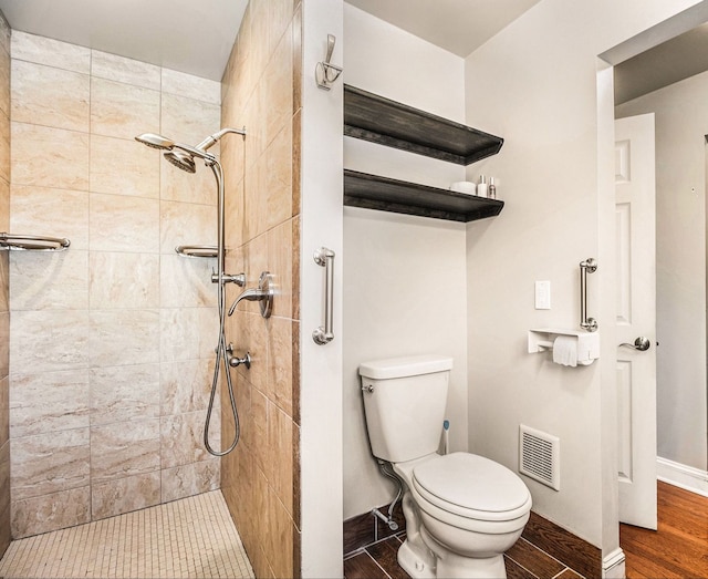 bathroom with toilet, baseboards, visible vents, and a tile shower