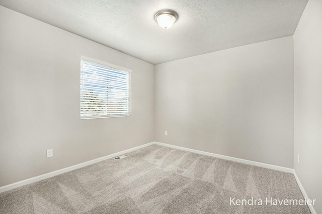 carpeted spare room featuring visible vents, baseboards, and a textured ceiling