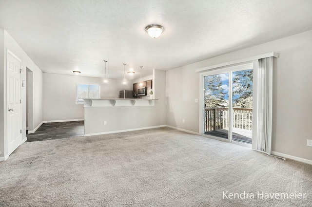 unfurnished living room featuring plenty of natural light, a textured ceiling, and dark carpet