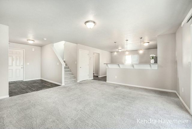 unfurnished living room featuring stairs, dark colored carpet, and baseboards