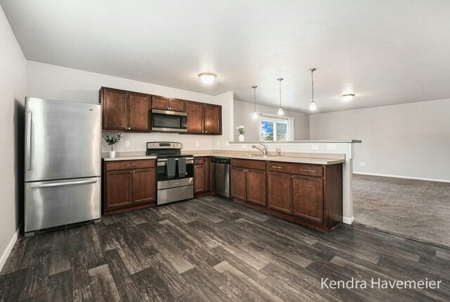 kitchen featuring a peninsula, a sink, light countertops, appliances with stainless steel finishes, and dark wood-style floors